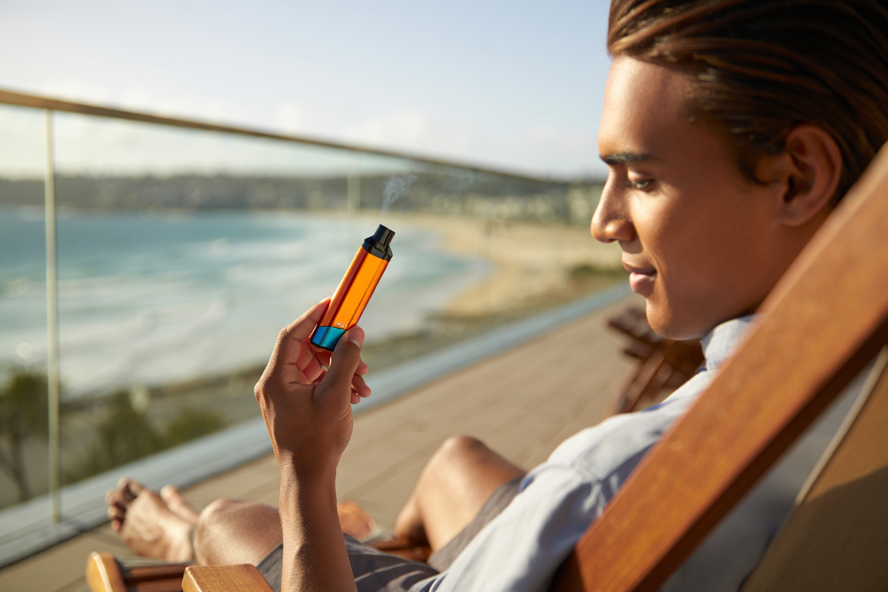 A person enjoying a vape outdoors with a scenic Australian background.